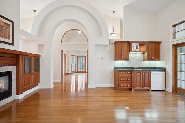 kitchen featuring dishwasher, hanging light fixtures, light hardwood / wood-style flooring, high vaulted ceiling, and a fireplace