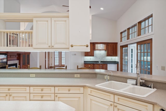 kitchen featuring backsplash, white dishwasher, sink, high vaulted ceiling, and cream cabinetry