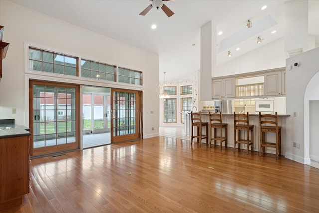 living room with ceiling fan, french doors, high vaulted ceiling, and light hardwood / wood-style flooring