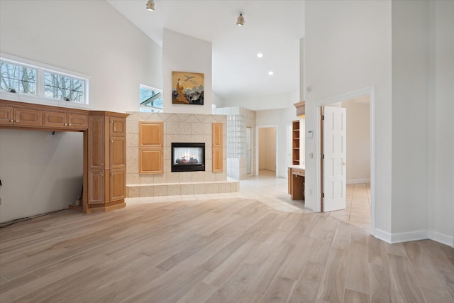 unfurnished living room featuring a towering ceiling, a tile fireplace, and light hardwood / wood-style flooring