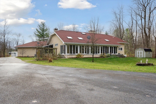 view of front of home featuring a sunroom, a front yard, and a storage shed