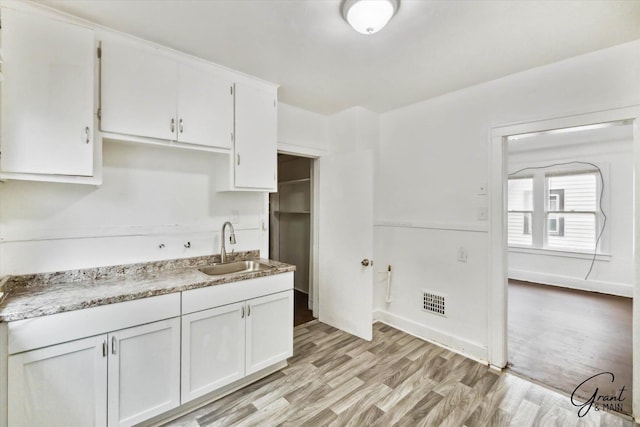 kitchen with light wood-type flooring, white cabinetry, and sink