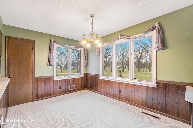 unfurnished dining area with carpet flooring, a notable chandelier, a textured ceiling, and wooden walls