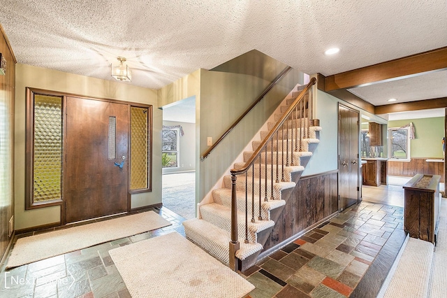 entryway with wooden walls, a healthy amount of sunlight, and a textured ceiling