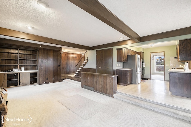 kitchen with wood walls, stainless steel fridge, a textured ceiling, beam ceiling, and dark brown cabinetry