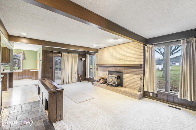 living room featuring beamed ceiling, a wood stove, a textured ceiling, and wooden walls