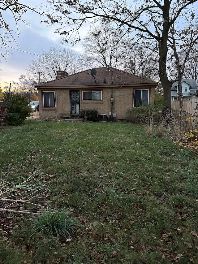 back house at dusk featuring a lawn and central air condition unit