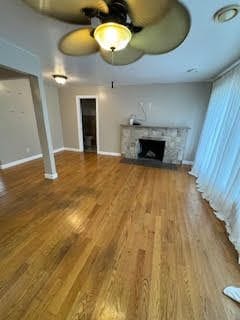 unfurnished living room featuring hardwood / wood-style flooring, ceiling fan, and a fireplace