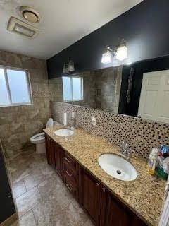 bathroom with decorative backsplash, vanity, toilet, and tile walls