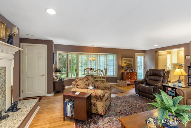 living room featuring a high end fireplace, light hardwood / wood-style floors, a wealth of natural light, and a chandelier