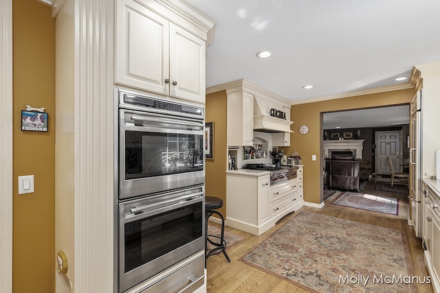 kitchen featuring premium range hood, white cabinets, light wood-type flooring, ornamental molding, and appliances with stainless steel finishes