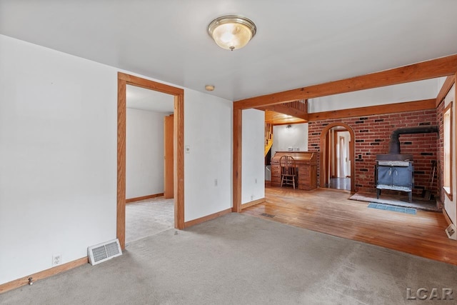 unfurnished living room with beam ceiling, light hardwood / wood-style flooring, and a wood stove