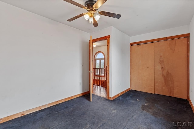 unfurnished bedroom with dark colored carpet, a closet, and ceiling fan