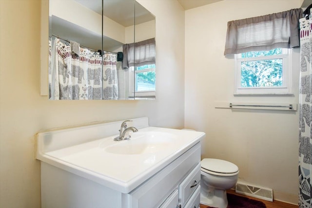 bathroom with wood-type flooring, vanity, a healthy amount of sunlight, and toilet