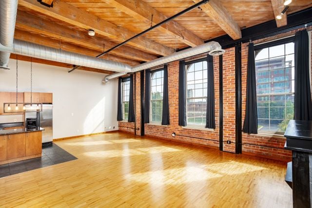 unfurnished living room with hardwood / wood-style floors, plenty of natural light, wood ceiling, and brick wall