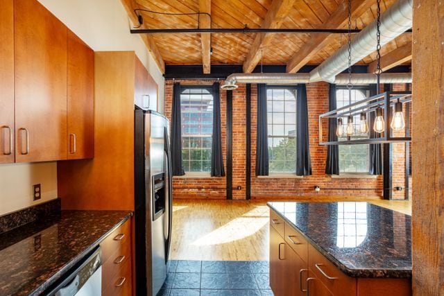 kitchen featuring stainless steel appliances, pendant lighting, wood ceiling, and brick wall