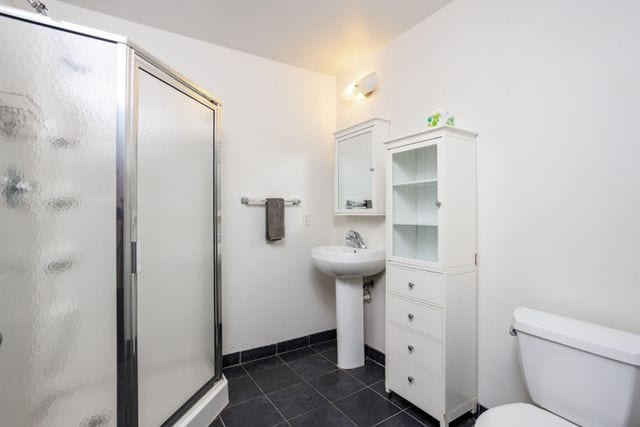 bathroom featuring tile patterned flooring, toilet, a shower with door, and sink