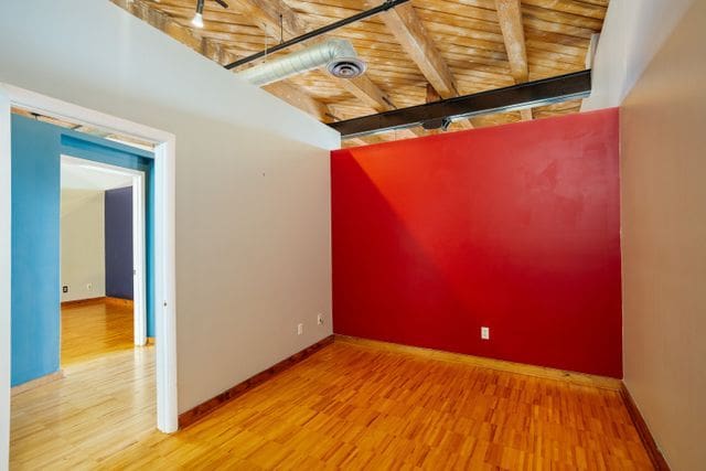 empty room with beam ceiling, wooden ceiling, and wood-type flooring