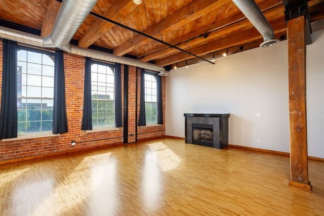 unfurnished living room featuring wood ceiling, a tile fireplace, brick wall, and light hardwood / wood-style flooring