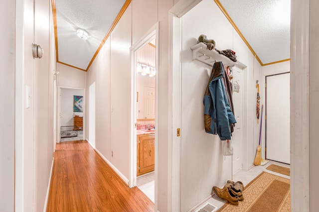 hall featuring crown molding, light wood-type flooring, a textured ceiling, and vaulted ceiling