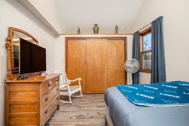 bedroom with light wood-type flooring, lofted ceiling, and a closet