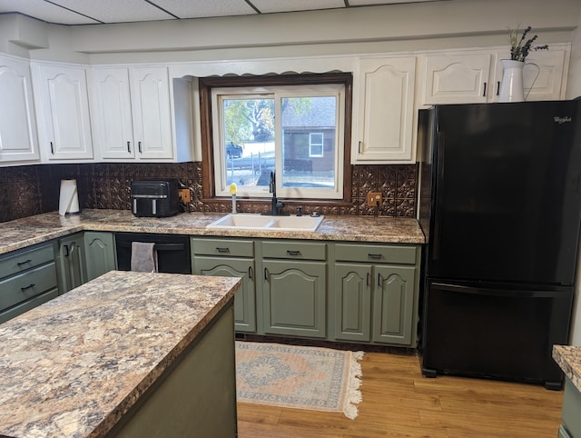 kitchen featuring white cabinets, a drop ceiling, black refrigerator, and sink