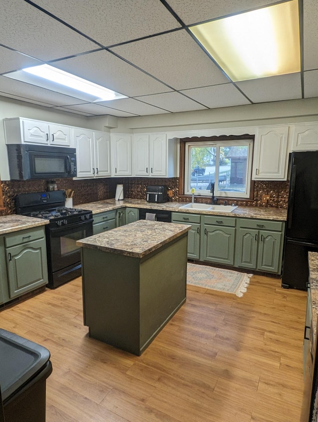 kitchen featuring a drop ceiling, black appliances, white cabinets, sink, and a kitchen island