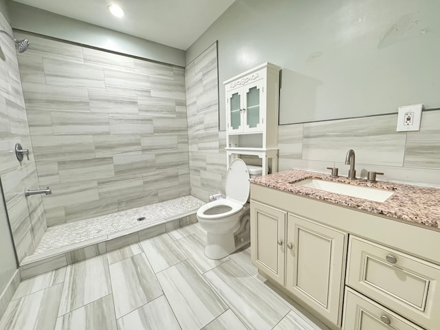 bathroom featuring tiled shower, vanity, toilet, and tile walls