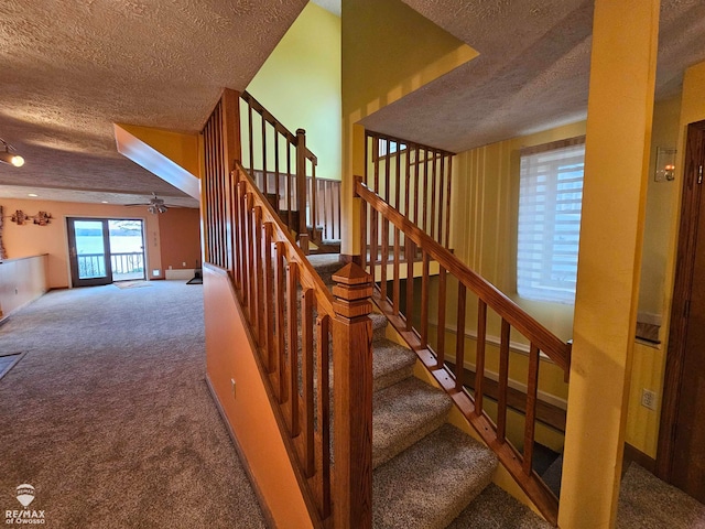 staircase with a textured ceiling, carpet floors, and ceiling fan