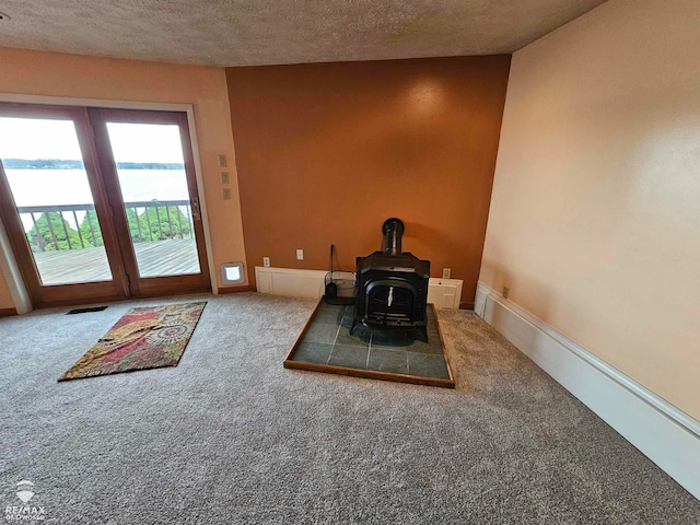 unfurnished dining area with carpet flooring, a textured ceiling, and a wood stove