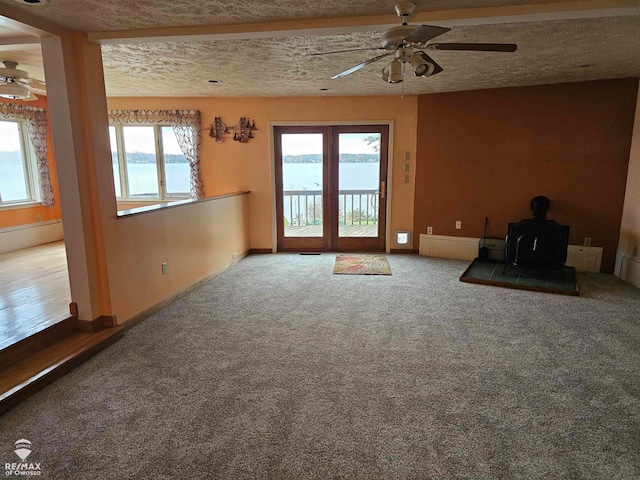 interior space with a wood stove, ceiling fan, a water view, and a textured ceiling