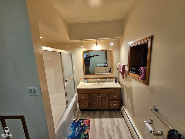 bathroom featuring hardwood / wood-style flooring, vanity, combined bath / shower with glass door, and a baseboard heating unit