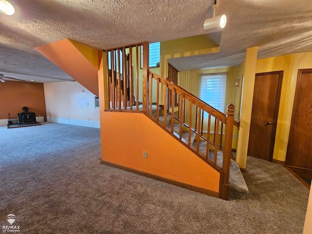 stairway with a wood stove, carpet floors, and a textured ceiling