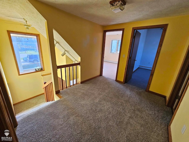 corridor with dark colored carpet, a textured ceiling, and baseboard heating