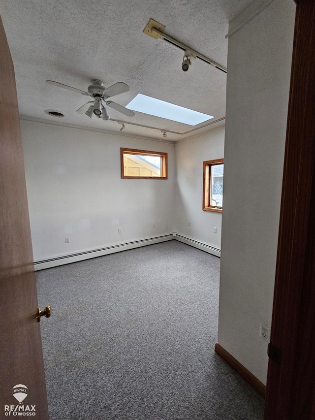 spare room with a baseboard heating unit, a skylight, ceiling fan, a textured ceiling, and carpet floors