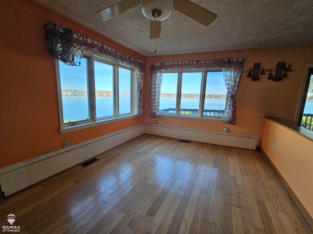 unfurnished room featuring ceiling fan, hardwood / wood-style floors, a water view, and a textured ceiling