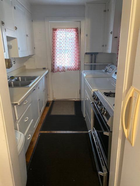 kitchen with electric stove, washer and clothes dryer, white cabinets, and sink