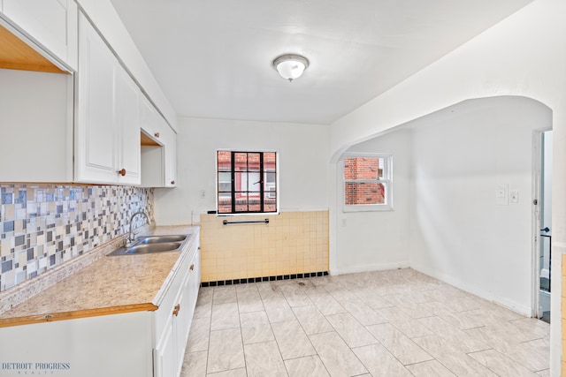 kitchen with white cabinetry, sink, and tile walls