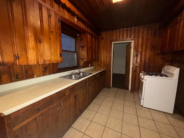 kitchen featuring white gas range, wooden walls, sink, and light tile patterned flooring