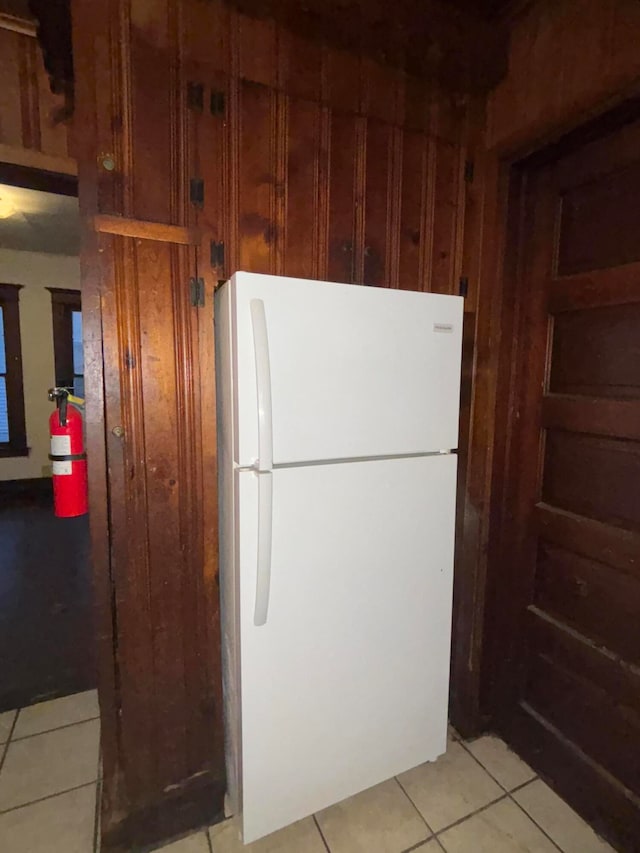 kitchen with white refrigerator, light tile patterned floors, and wooden walls