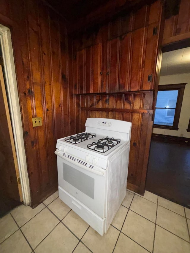 kitchen with wood walls, light tile patterned floors, and white range with gas stovetop