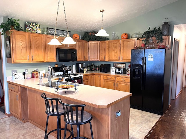 kitchen featuring hanging light fixtures, kitchen peninsula, a textured ceiling, black appliances, and light wood-type flooring