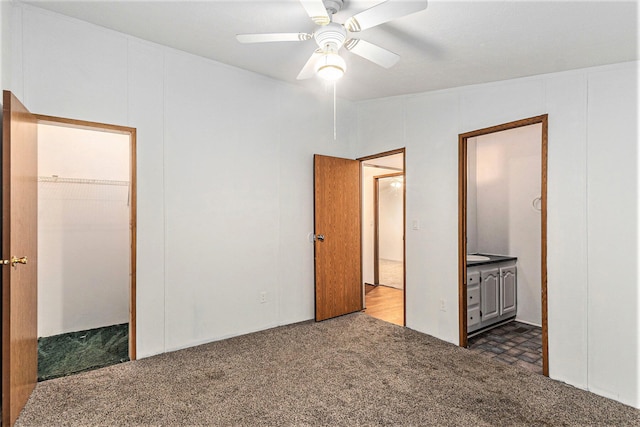 unfurnished bedroom featuring ceiling fan, dark carpet, and ensuite bath