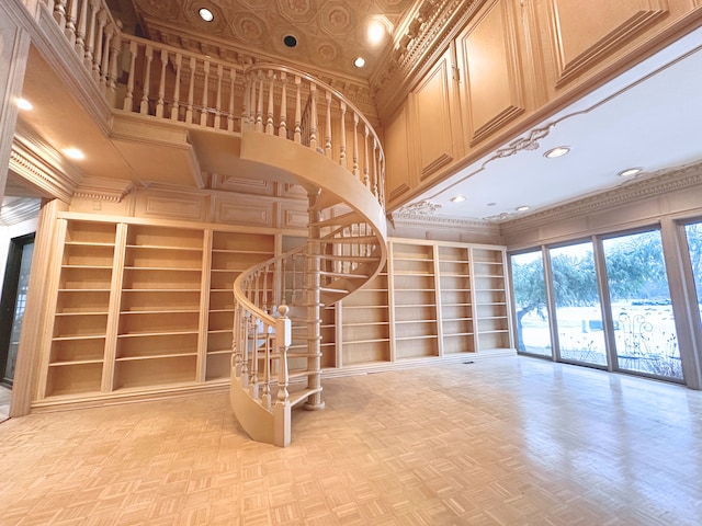 unfurnished living room featuring built in shelves, a towering ceiling, ornamental molding, and light parquet floors