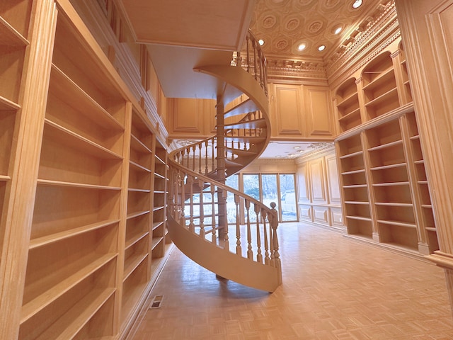 stairway with ornamental molding, parquet floors, and built in shelves