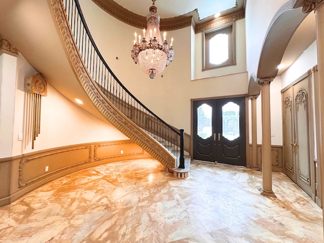 foyer entrance with a notable chandelier, a towering ceiling, french doors, and ornate columns