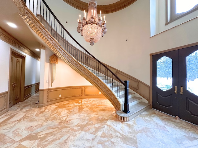 foyer featuring a notable chandelier, a towering ceiling, ornamental molding, and french doors