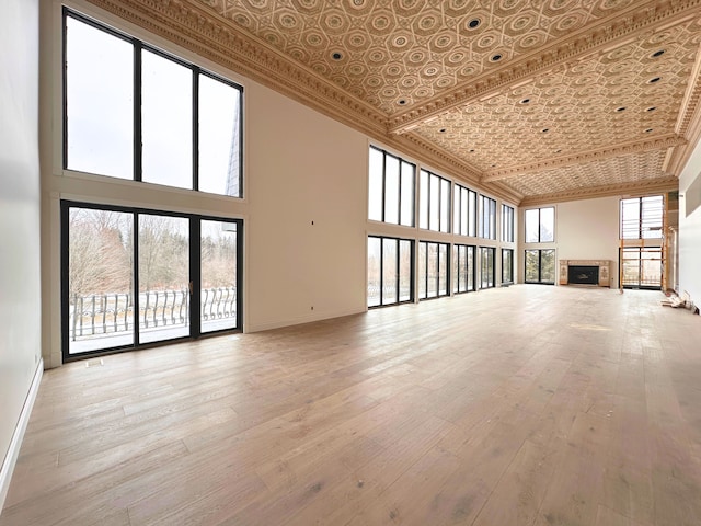 unfurnished living room featuring crown molding, a towering ceiling, a wealth of natural light, and light hardwood / wood-style floors