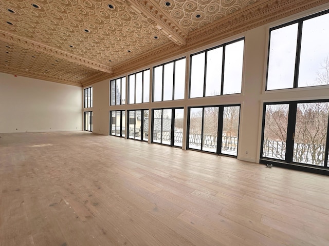 unfurnished room with crown molding, a towering ceiling, and light wood-type flooring