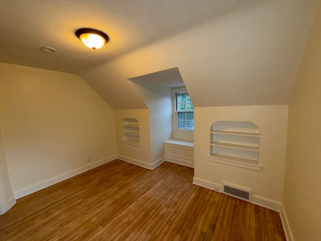 additional living space featuring built in shelves, hardwood / wood-style flooring, and vaulted ceiling